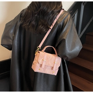 Detail van een roze crossbodytas met textuur en gouden hardware gedragen door een model