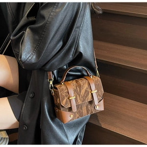 Detail van vintage bruine crossbodytas met textuur en gouden metalen gespen en riemen