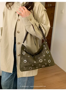 Macro detail of dark green suede handbag with metallic eyelets and brown leather handle