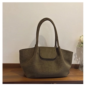 Detalle de bolso tote grande de ante verde oliva en mesa de madera con decoración floral