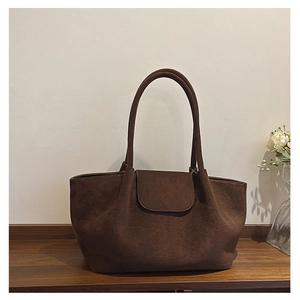 Detalle de un bolso tote grande en ante marrón oscuro con solapa minimalista y asas finas