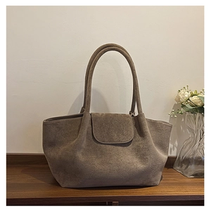 Textura detallada de un bolso tote de ante topo con solapa frontal minimalista en un estante
