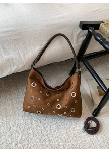Detail shot of brown suede bag with silver metal eyelets on a decorative rug