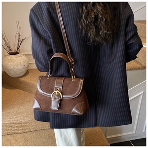 Detail view of dark brown suede and leather saddle bag worn by a model on stairs