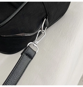 Detail van zilveren karabijnsluiting en lederen riem op zwarte suède avondtas voor dames