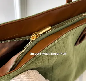 Close-up of golden zipper puller on green quilted suede tote with brown leather trim