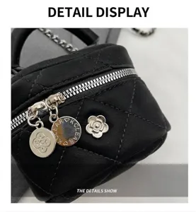 Detalle del bolso acolchado negro con cadena, cremallera plateada y dije de camelia