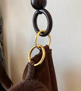 Close-up of durable golden metal hooks and dark round handle on brown suede tote bag