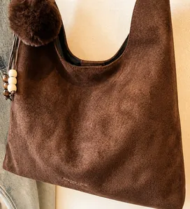 Detail of dark brown suede tote bag with plush pompom and wooden bead charm accent