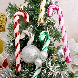 Close-up of glittery striped candy canes and silver baubles hanging on a green Christmas tree