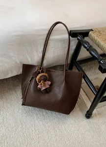 Gros plan sur un sac cabas marron avec charme d'ours et texture en cuir grainé