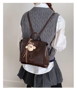 Detalle de la mochila vintage marrón oscuro con logotipo grabado y amuleto de osito de peluche