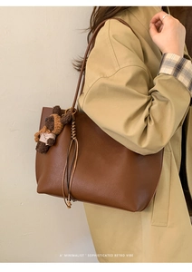 Sac cabas en cuir marron grainé avec pendentif ours porté avec un trench-coat classique