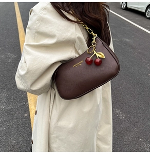 Détail du sac en cuir grainé marron foncé avec chaîne dorée et breloque cerise