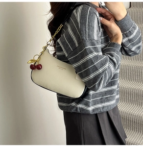 Sac à bandoulière chic en cuir crème avec chaîne dorée et charm cerise sur modèle