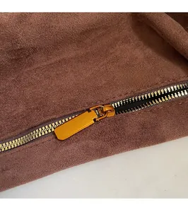 Detailed macro view of dark brown suede bag with gold zipper and stitching