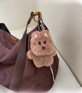 Close-up of fluffy brown dog plush keychain with TOP DOG bone tag on suede handbag
