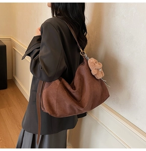 Detail of a large brown suede crossbody bag with metal rings and a cute bear charm
