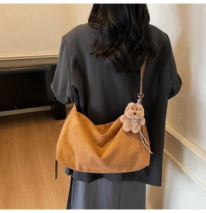 Brown suede hobo bag on shoulder showing large capacity and decorative bear pendant
