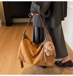 Detail of suede crescent bag in caramel brown featuring a cute plush dog charm