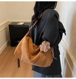 Close-up of a brown suede hobo bag with a cute plush bear pendant and wide shoulder strap