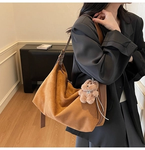 Detail of large brown suede hobo bag with teddy bear charm worn by a model in black blazer