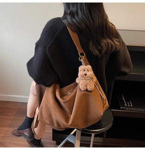 Detailed view of the brown suede crossbody bag with a plush bear charm on a model's back