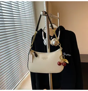 Détail du sac baguette en cuir crème avec chaîne dorée et breloque cerise rouge