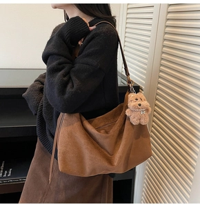 Detail view of a brown suede hobo bag with a plush bear charm on a female model