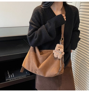 Detail of a brown suede slouchy crossbody bag with a plush bear charm on a wide strap