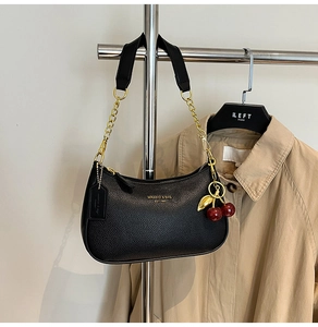 Détail d'un sac hobo en cuir grainé noir avec chaîne dorée et breloque cerise élégante
