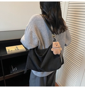 Detail of black large capacity shoulder bag with a cute plush bear pendant on a model