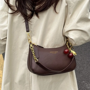 Sac demi-lune en cuir marron foncé avec chaîne dorée et cerise porté par une femme