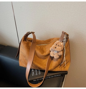 Detail of caramel suede hobo bag featuring a wide strap and plush dog keychain