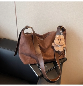 Detail of dark brown suede tote bag with leather strap and plush bear charm on a sofa