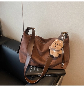 Detail of dark brown suede crossbody bag with wide strap and plush bear charm decoration