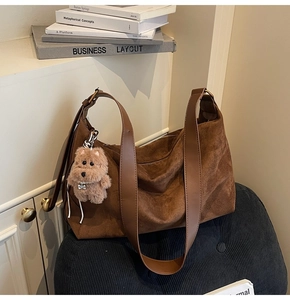 Brown suede tote bag with leather strap and plush dog charm in a minimalist setting
