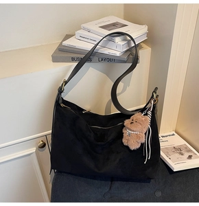Detail of black suede shoulder bag with brown plush bear charm and leather strap