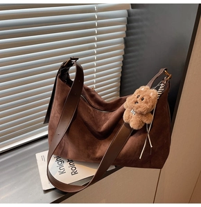 Detail of soft dark brown suede hobo bag with wide leather strap and cute bear charm