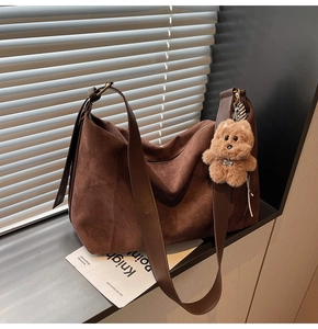 Detail of a large brown suede hobo bag with wide shoulder strap and cute puppy pendant