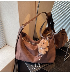 Detail of a brown suede hobo bag with a plush bear charm and metallic hardware