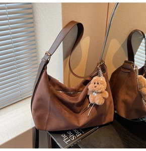 Macro detail of dark brown faux suede tote bag featuring a cute plush bear charm accessory