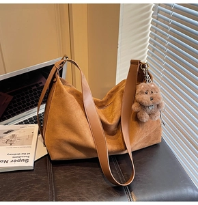 Brown suede tote bag with leather strap and plush bear charm in a home office setting