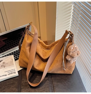 Detail of tan faux suede tote bag with plush bear charm and woven tassel detail