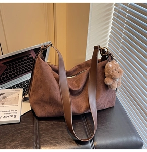 Detail of a brown suede hobo bag with wide shoulder strap and a cute plush bear pendant