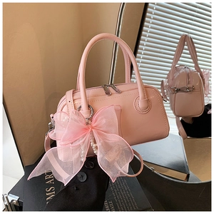 Détail du sac polochon rose verni avec grand nœud en dentelle et pendentif perle élégant