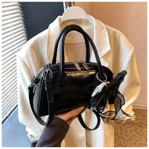Détail du sac Boston noir verni avec pendentif perle et bandoulière ajustable