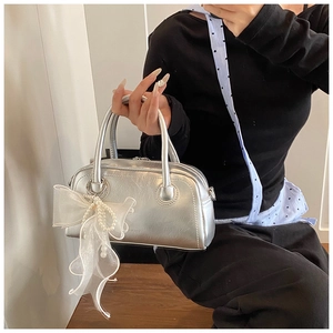 Détail du sac polochon argenté avec nœud en organza blanc et élégante chaîne en perles