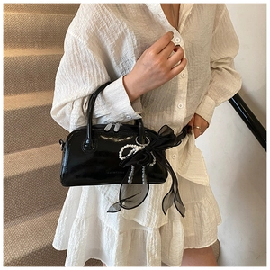 Détail du sac à main noir brillant avec chaîne en perles et nœud en tulle délicat