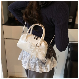 Détail du sac polochon blanc brillant avec nœud en dentelle et perles sur le modèle